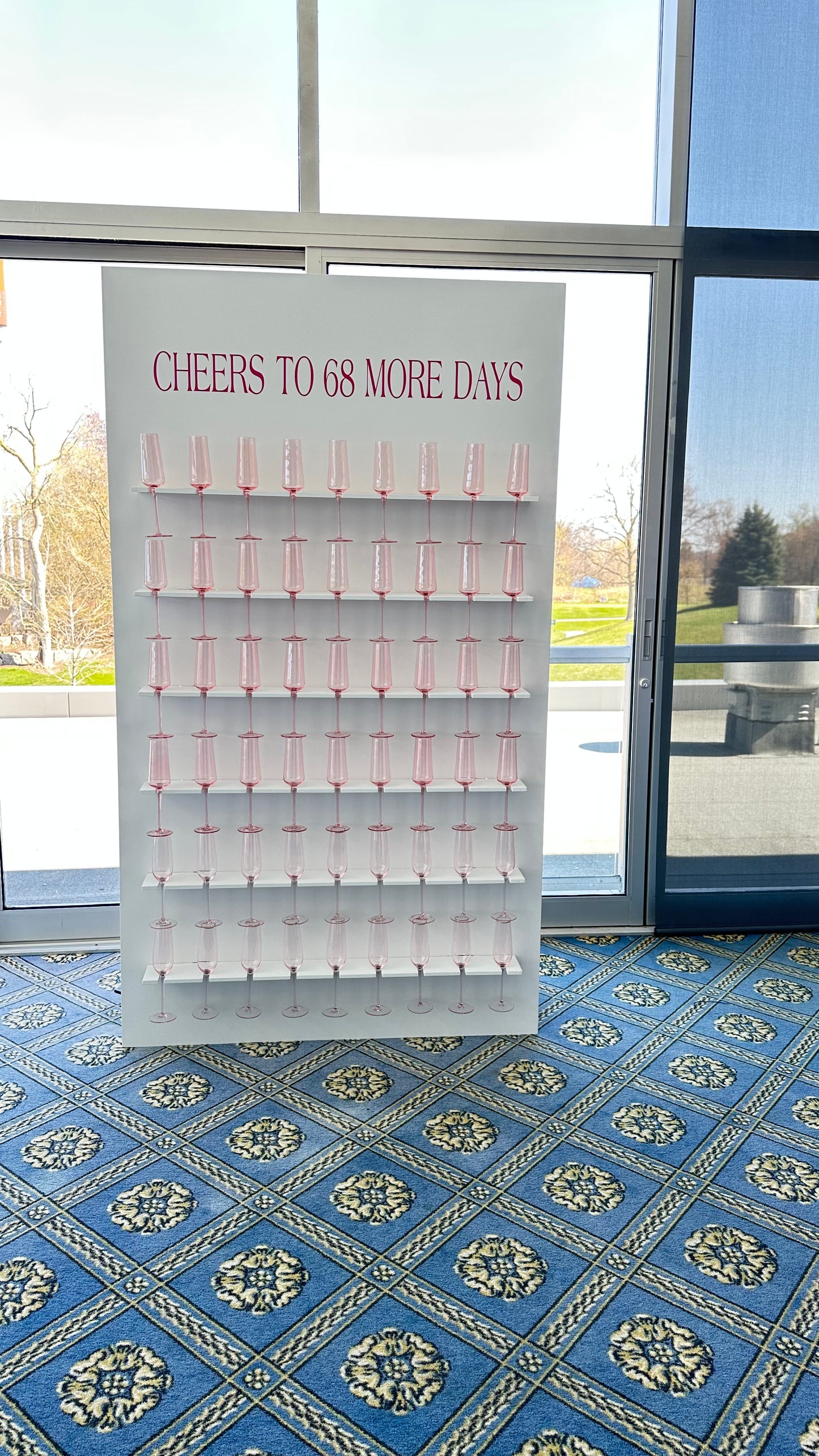 Display board with 'Cheers to 68 More Days' text in a room with large windows.