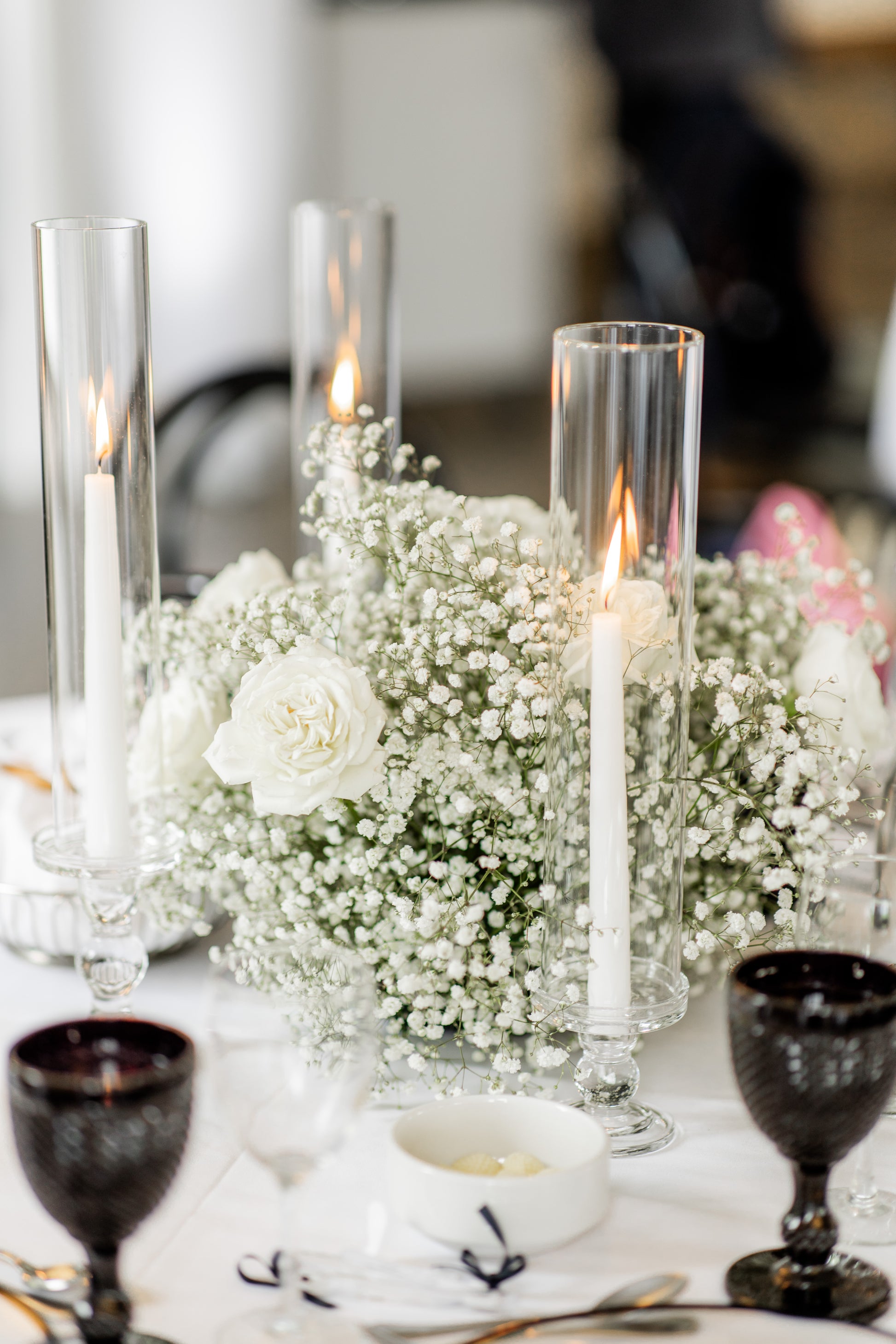 Table setting with candles, flowers, and glasses on a white tablecloth.