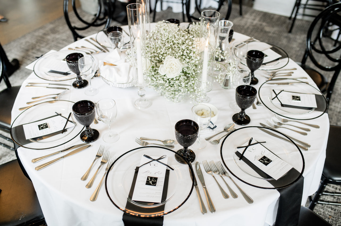 Elegant table setting with black and white plates, gold cutlery, and centerpieces.