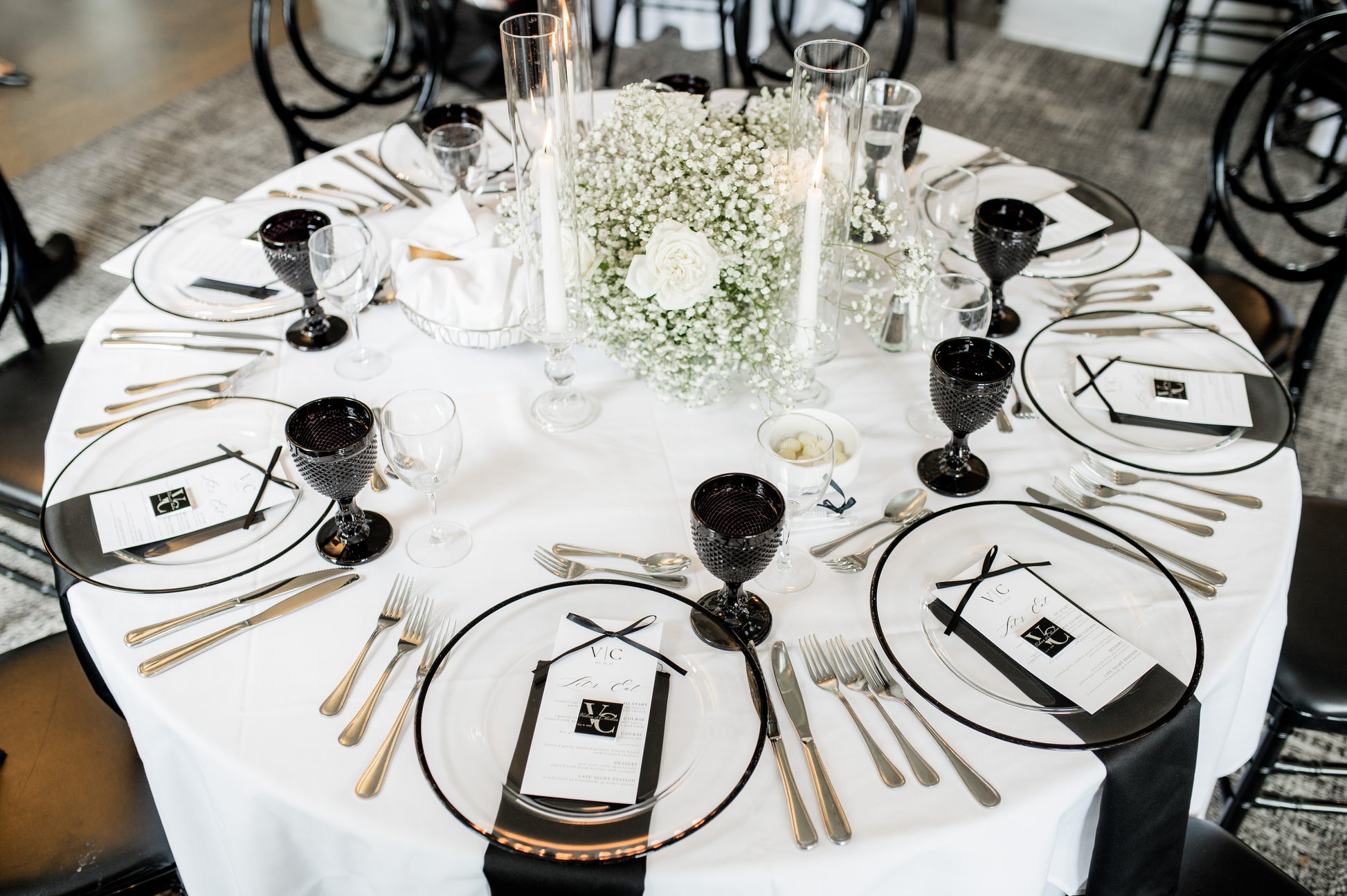 Elegant table setting with black and white plates, gold cutlery, and centerpieces.