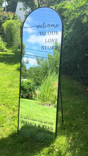 Decorative mirror with 'Welcome to Our Love Story' text in a garden setting