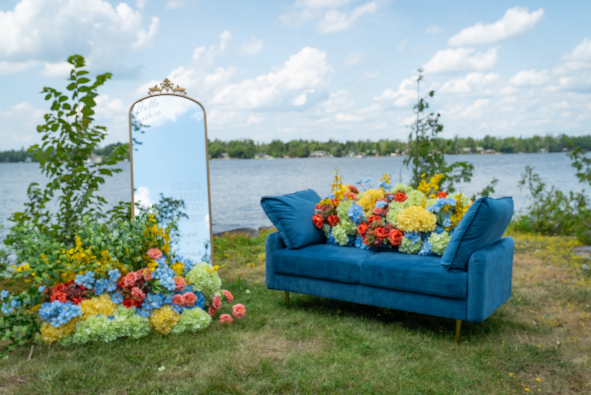 Blue sofa with colorful flowers and a large mirror outdoors by a lake.