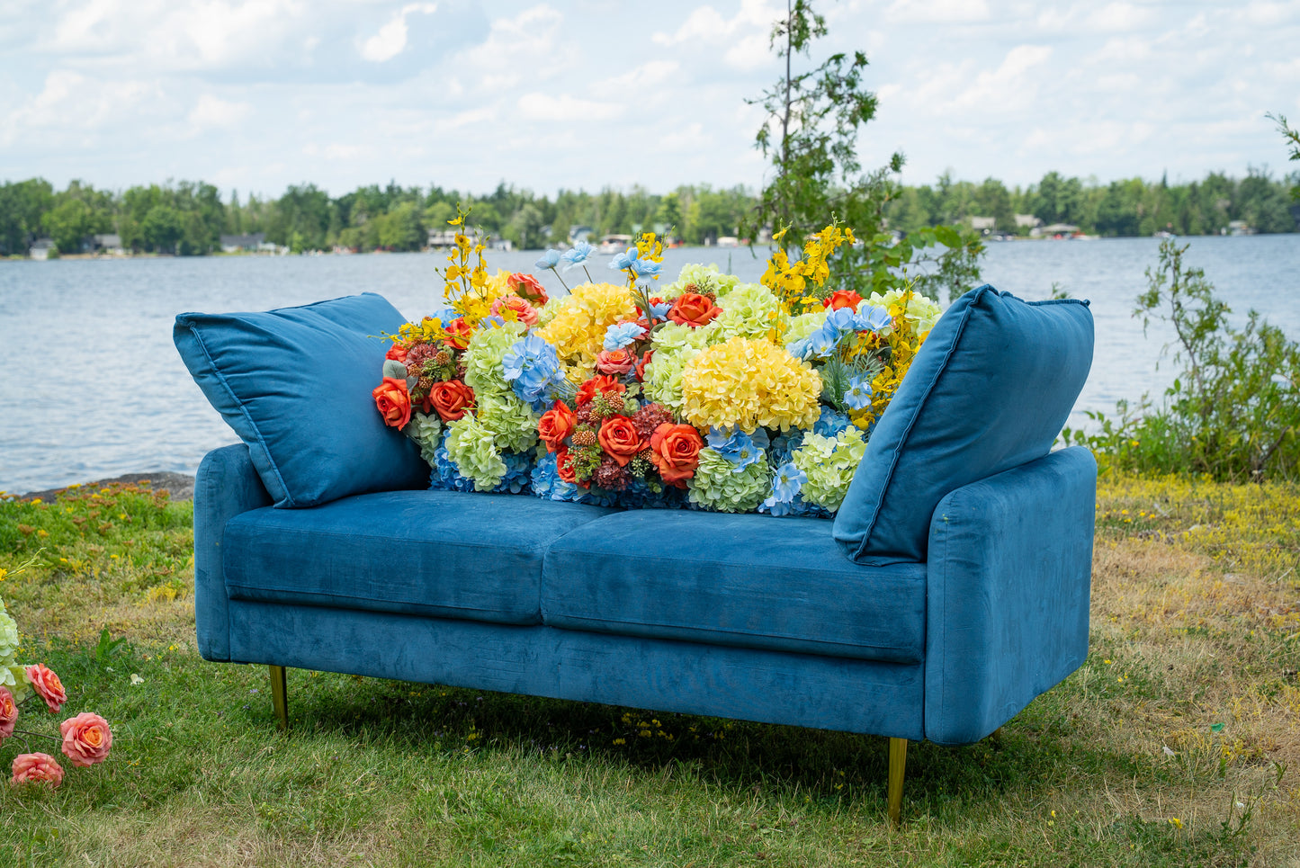 Blue sofa with colorful flowers on a grassy area near a body of water.