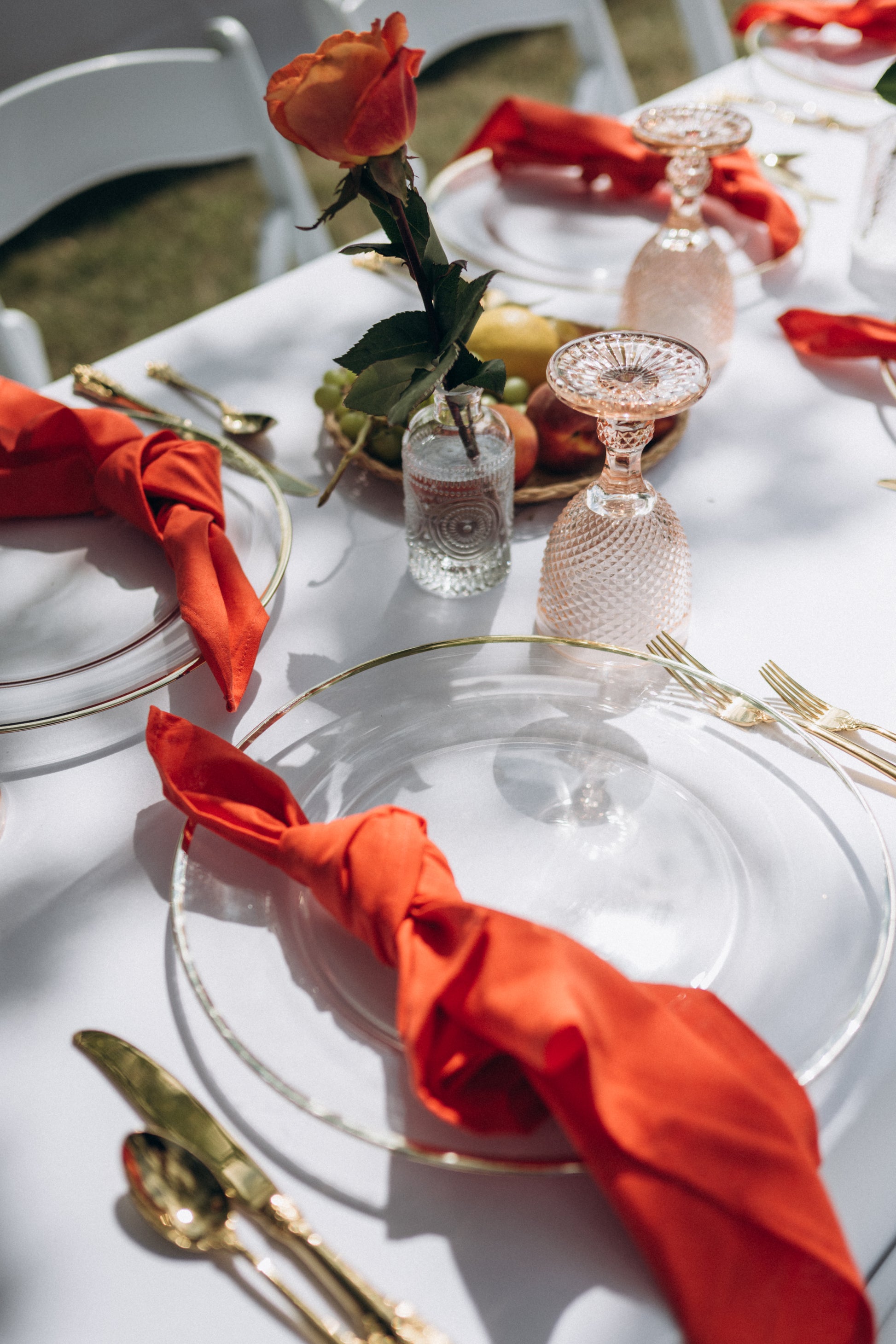 Elegant table setting with red napkins, gold cutlery, and clear glassware on a white tablecloth.