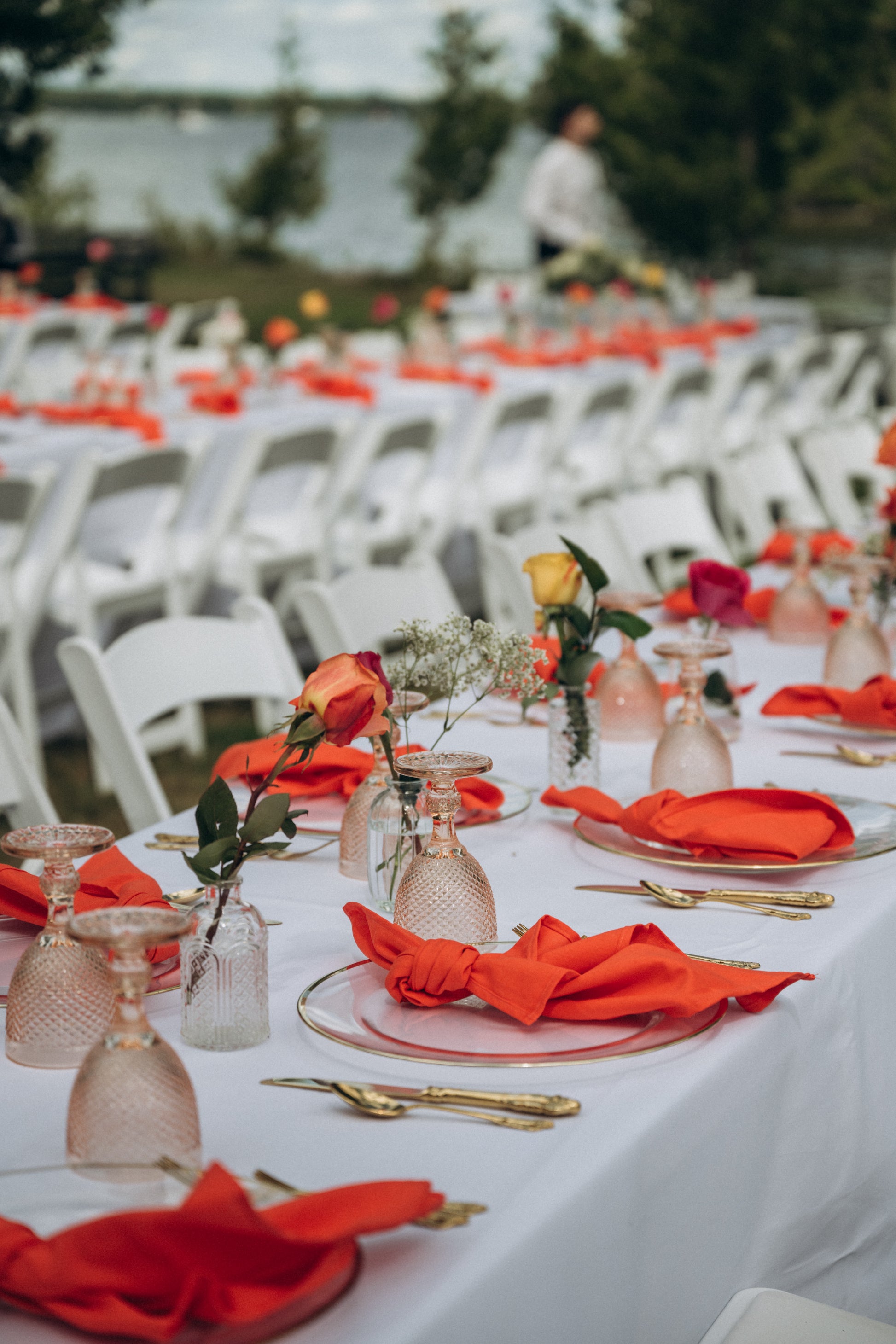 Decorated tables with red napkins and clear glassware at an outdoor event.