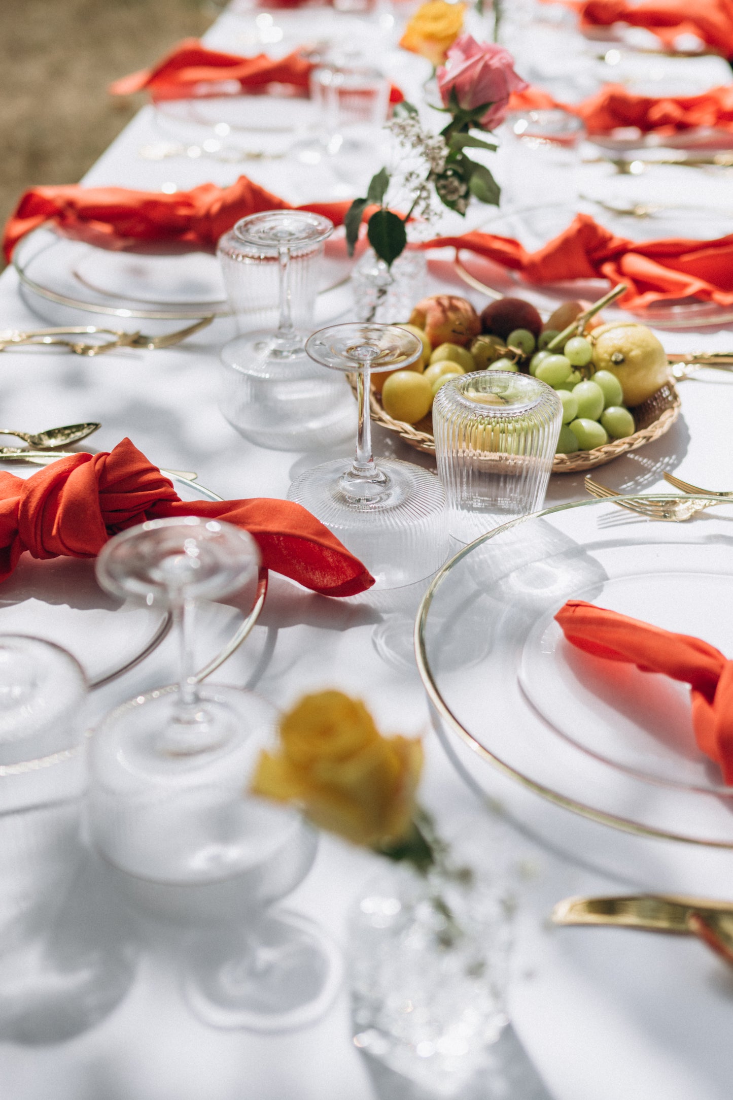 Elegant table setting with red napkins, white tablecloth, and fruit centerpiece.