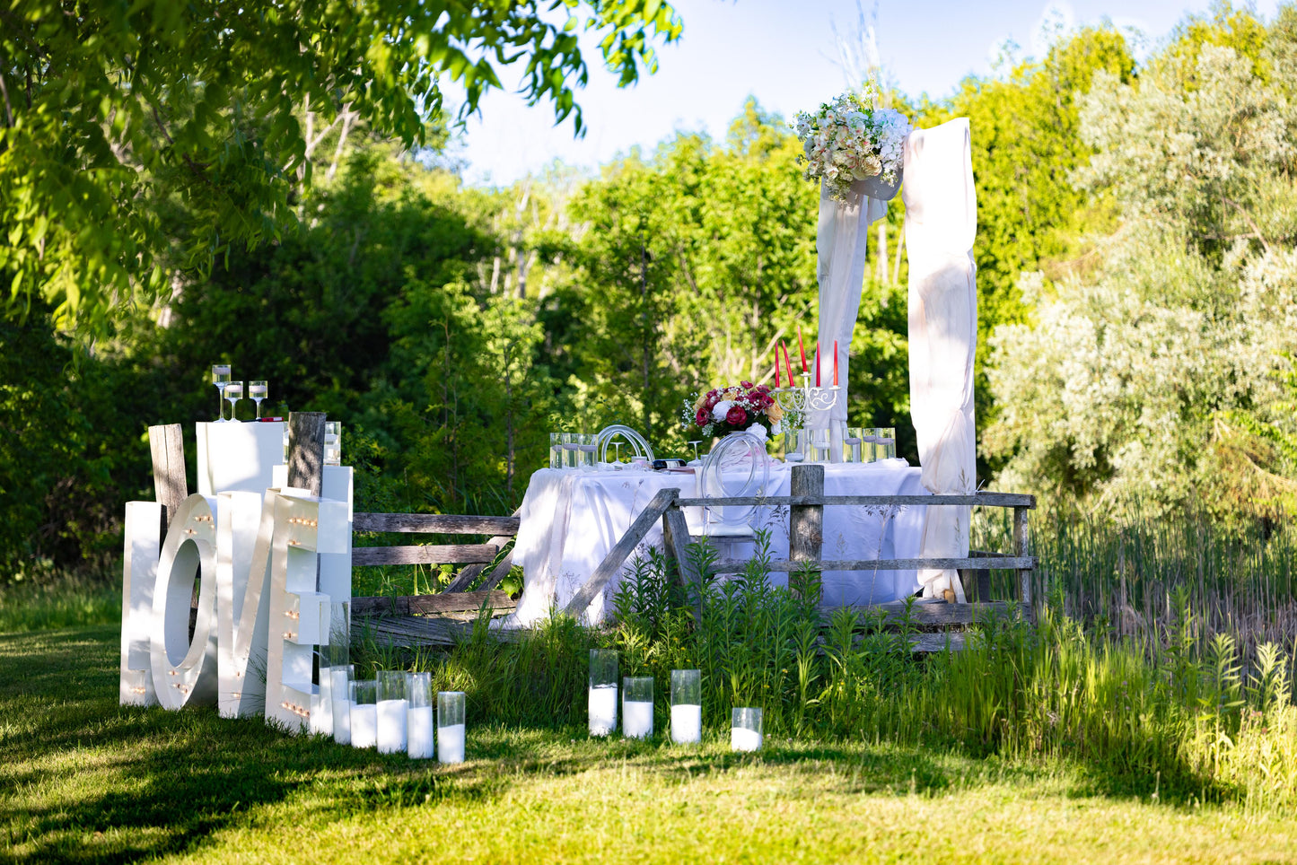 Outdoor wedding setup with a table, chairs, and 'LOVE' letters in a garden.